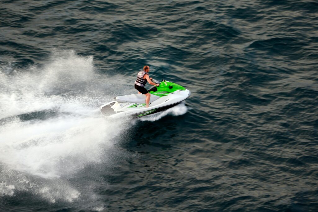 A man on a green and white jet ski speeding across the ocean on a sunny day.
